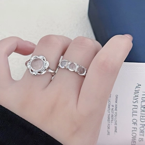 Macro view of silver rings featuring a flower-shaped pink gemstone and triple-stone band
