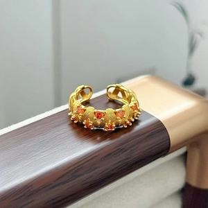 Dettaglio di anello vintage dorato con trama intrecciata e zirconi arancioni brillanti