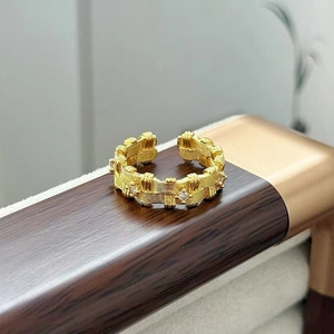 Dettaglio di un anello vintage dorato con trama intrecciata e zirconi su legno