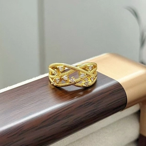 Dettaglio macro di anello intrecciato dorato con zirconi bianchi su supporto in legno