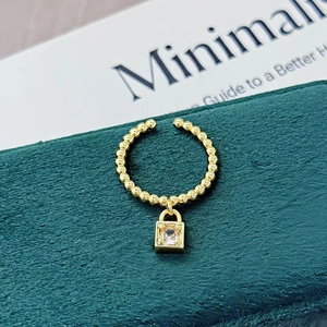 Nahaufnahme einer goldenen Perlen-Ohrklemme mit quadratischem Schloss-Anhänger auf Samt