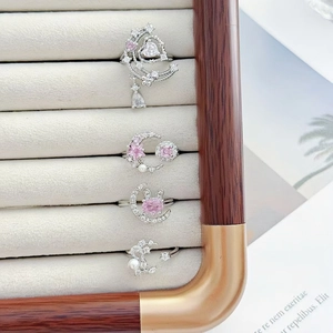 Dettaglio di quattro anelli d'argento con zirconi rosa e perle su velluto beige