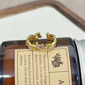 Detailansicht eines Goldrings mit violetten Emailleherzen auf einer Vintage-Glasflasche