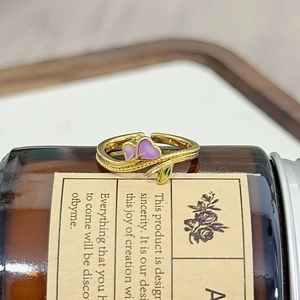 Makroaufnahme von vergoldetem Herzring mit lila Emaille und grünen Blattdetails