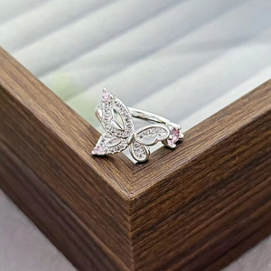 Macro detail of silver butterfly ring with pink zircons on a wooden jewelry box
