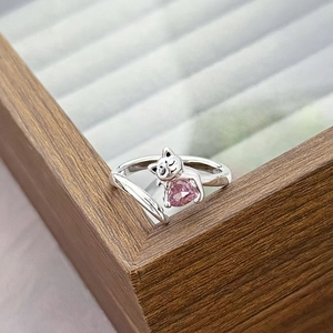 Detail of an adjustable cat ring featuring a pink heart-shaped zircon on a wooden display