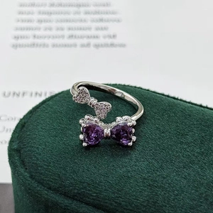 Close-up of silver ring with purple heart-shaped stones and pavé bow on velvet box