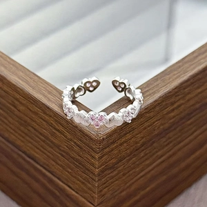 Close-up of adjustable silver heart ring with sparkling pink zircons on wood box