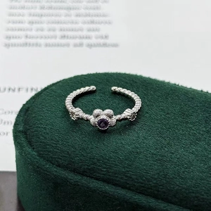 Close-up of a silver plum blossom ring with purple gemstone on a green velvet stand