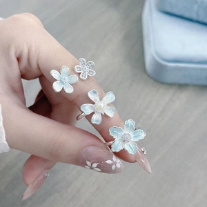 Nahaufnahme von vier Emaille-Blumenringen mit Perlen und Zirkonia an der Hand