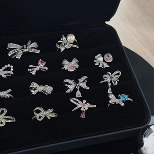 Detailed view of silver bow rings with colorful zircon stones and pearls in a black tray