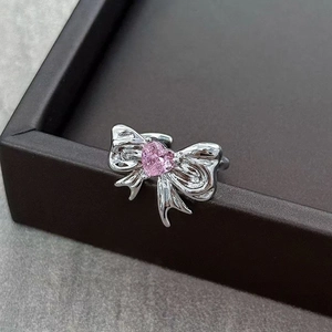 Macro view of silver bow ring with pink heart-shaped zircon on a dark stone surface