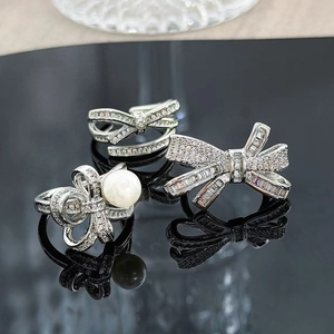 Close-up of silver bow rings with sparkling cubic zirconia and a white pearl on mirror