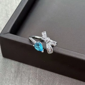 Macro detail of silver bow ring with pear-shaped blue gemstone and micro-pave crystals