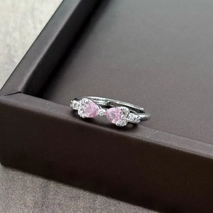 Macro shot of silver bow ring with pink heart stones and zircon accents on a display box