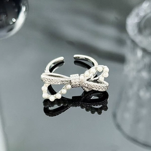 Detail of silver bow ring featuring pavé zircons and white pearls on a dark background