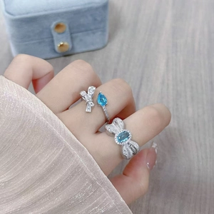 Macro detail of silver-toned bow rings with light blue zircon and silk texture band