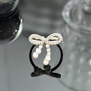 Detail of silver bow ring with sparkling zircons and dangling white pearl charms