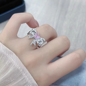 Detail of silver bow ring featuring a pink heart stone on a model's index finger