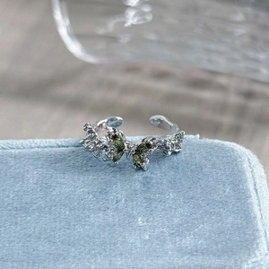 Macro detail of silver butterfly ring with green stones and sparkling pavé diamonds