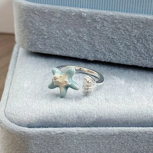 Nahaufnahme eines silbernen Rings mit hellblauem Emaille-Seestern und Muschel-Detail