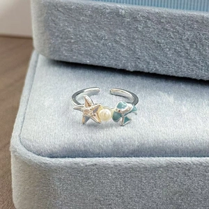 Nahaufnahme von Emaille-Ring mit Seestern und Perle auf blauem Samt-Schmuckkästchen
