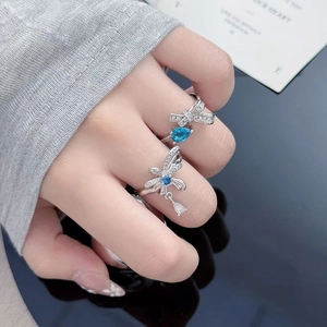 Close-up of bow ring featuring a large blue teardrop zircon and dainty silver-tone charms