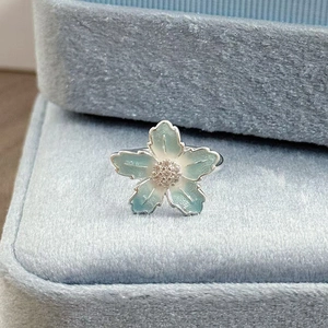Makroaufnahme eines Emaille-Blumenrings mit Zirkonia auf blauer Samtbox
