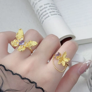 Nahaufnahme eines goldenen Schmetterlingsrings mit lila Zirkon und feiner Perlenkette