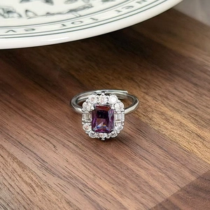 Macro detail of rectangle purple zircon ring with shimmering crystal halo on wood