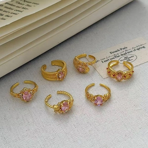 Dettaglio di anelli dorati vintage con gemme rosa ovali e incisioni ornamentali raffinate