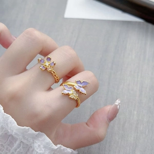 Vintage gouden ringen met paarse emaille bloemen en vlinders aan een vrouwenhand