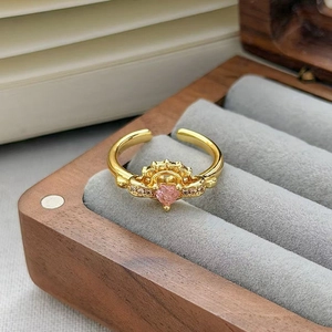 Dettaglio macro dell'anello a corona dorato con cuore rosa su scatola velluto