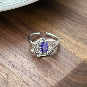 Macro shot of silver ring with oval purple zircon and side diamonds on wood