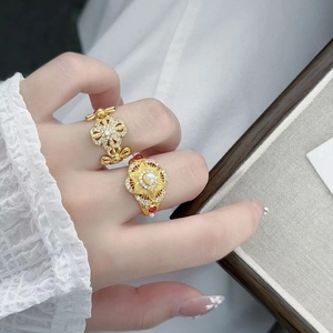 Détail de bagues vintage dorées avec perle blanche et pierre rouge sur fond de dentelle