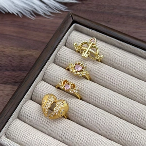 Vista dettagliata di quattro anelli vintage dorati con zirconi rosa e ciondoli a cuore
