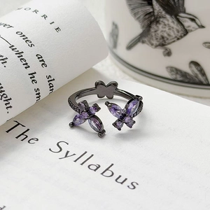 Vue détaillée de la bague papillon sombre avec zircons violets posée sur un livre