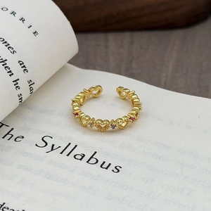 Macro di un anello vintage in oro con cuori traforati e zirconi colorati su un libro