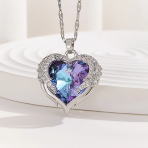 Blue crystal heart necklace with silver angel wings on white platform background