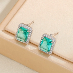 Detail view of emerald-cut green gemstone earrings with a sparkling zircon halo on a gold box