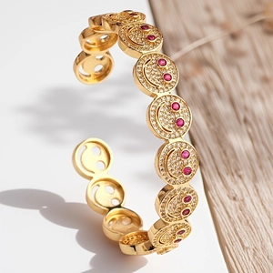 Detailansicht eines goldenen Armreifs mit Zirkonia-Smileys und roten Edelsteinakzenten