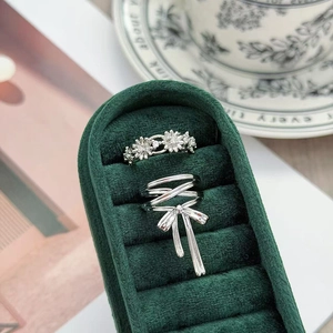 Dettaglio del set di anelli in argento con fiocco e margherite in scatola di velluto verde