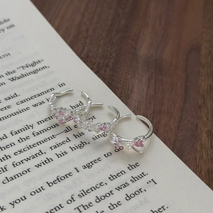 Detail of silver bow and heart rings with pink zircons and pearls on book pages