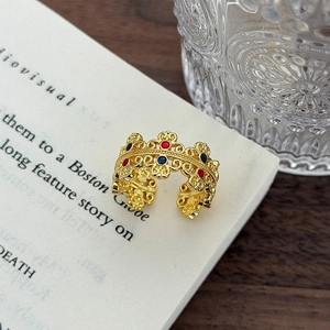 Dettaglio di anello dorato stile vintage con motivo a corona traforato e smalto colorato