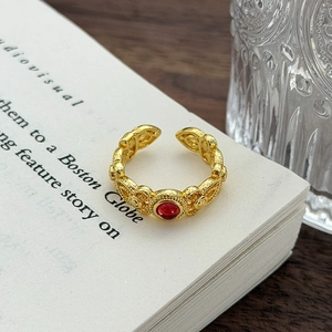 Dettaglio dell'anello vintage dorato con zircone rosso e motivi traforati eleganti