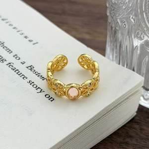 Dettaglio anello dorato traforato con pietra rosa centrale e piccoli strass