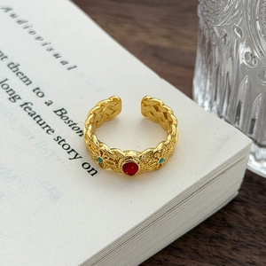 Dettaglio di anello vintage regolabile con pietra rossa e smalto turchese su libro aperto