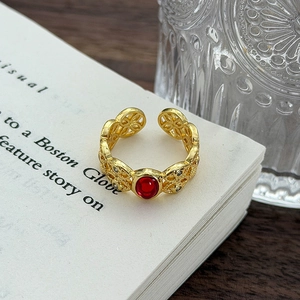 Dettaglio anello vintage dorato con motivi floreali traforati e gemma rossa