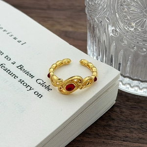 Dettaglio anello vintage in smalto dorato con gemma rossa su pagine di un libro