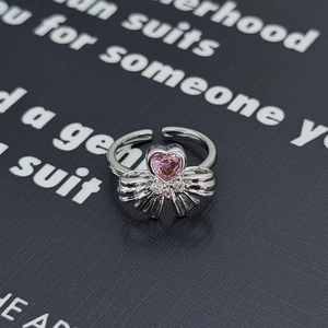 Dettaglio macro di un anello d'argento con gemma cuore rosa e fiocco su sfondo nero